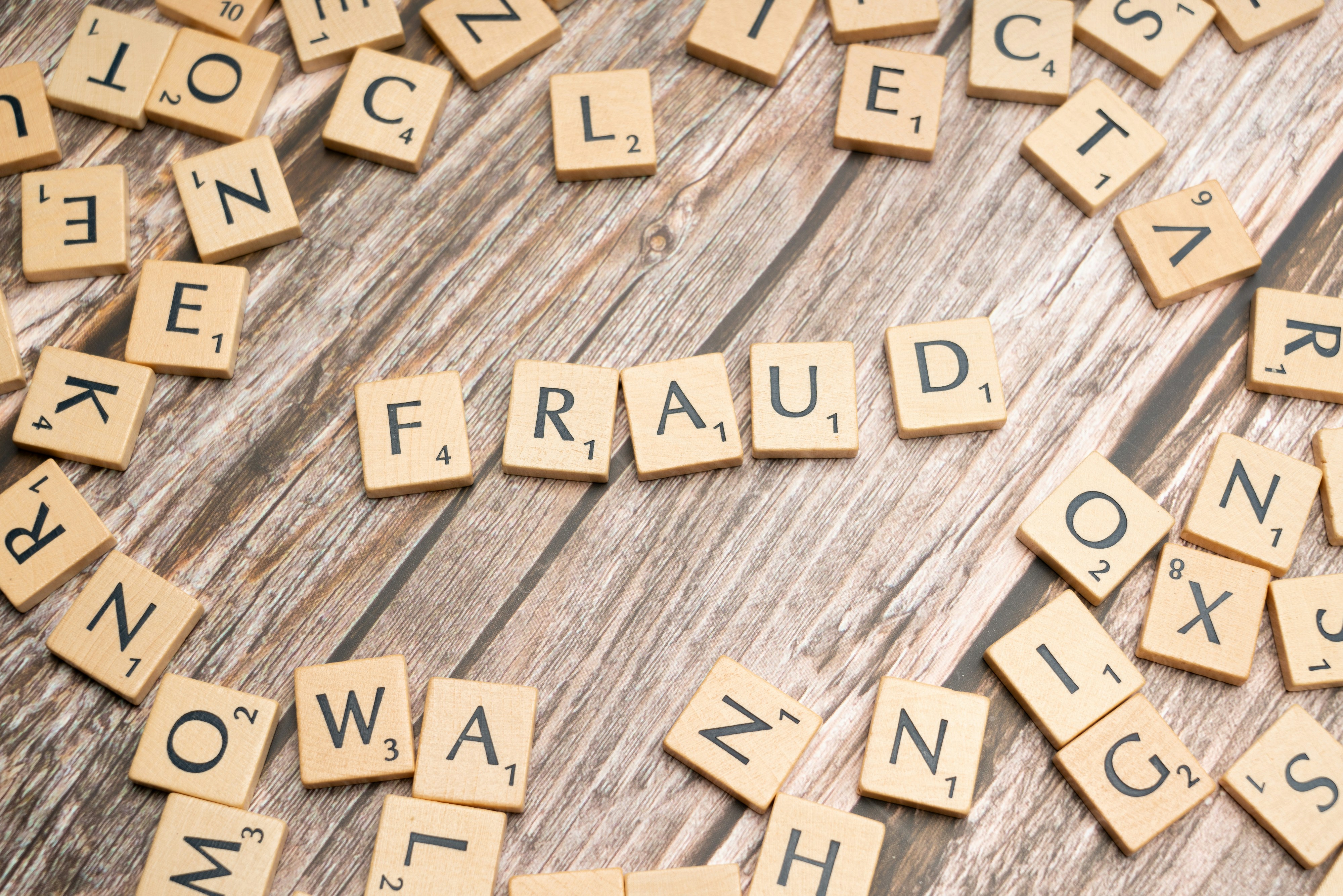 Scrabble-style letter tiles arranged to spell the word “fraud” on a wooden surface, symbolising complex fraud investigations.